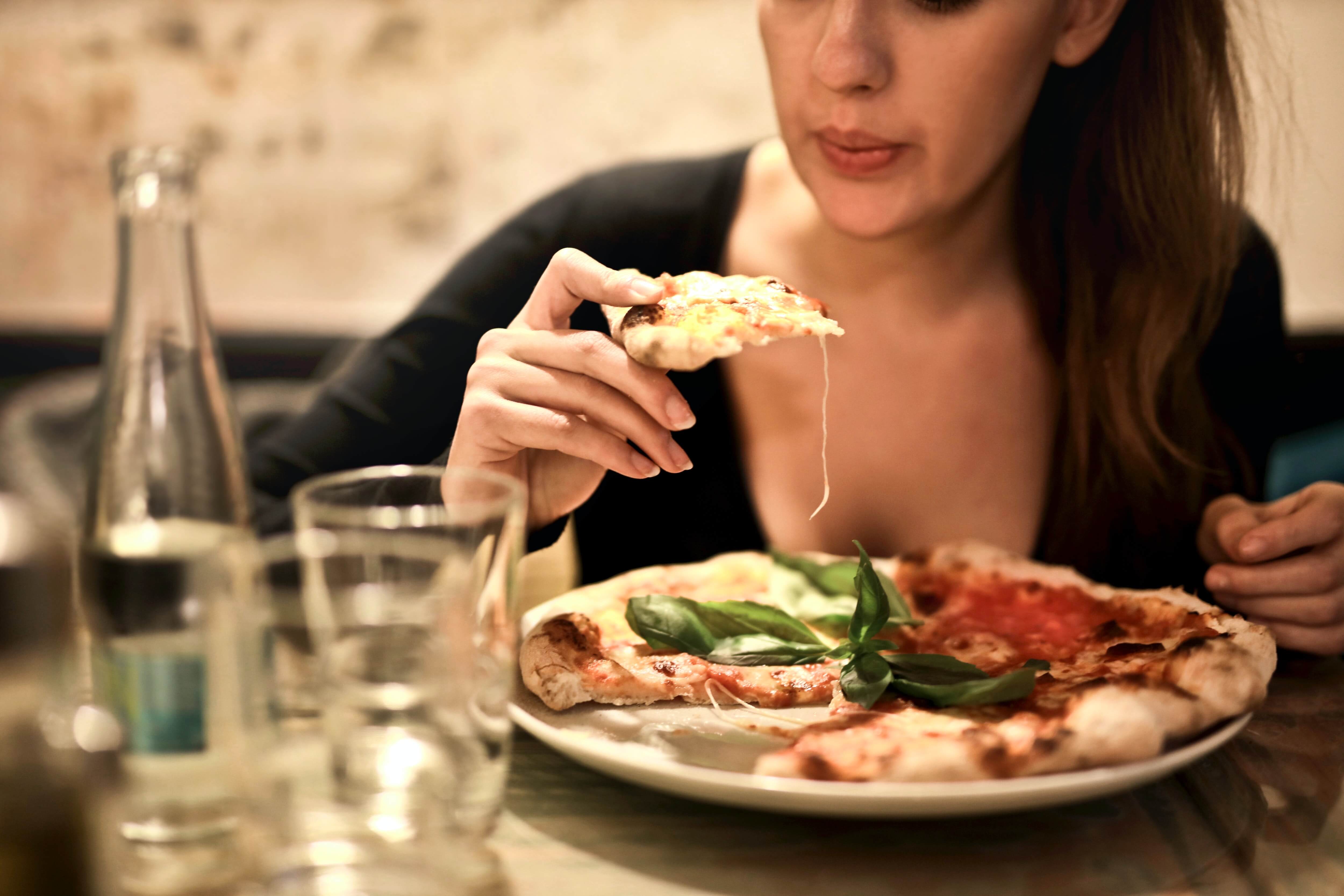 woman-holds-sliced-pizza-seats-by-table-with-glass-723031.jpg